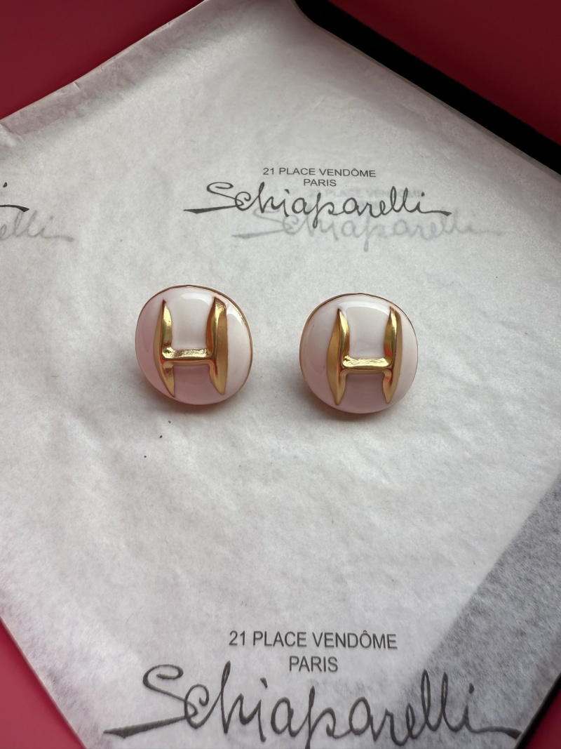 Серьги с золотым логотипом H на белом фоне Schiaparelli
