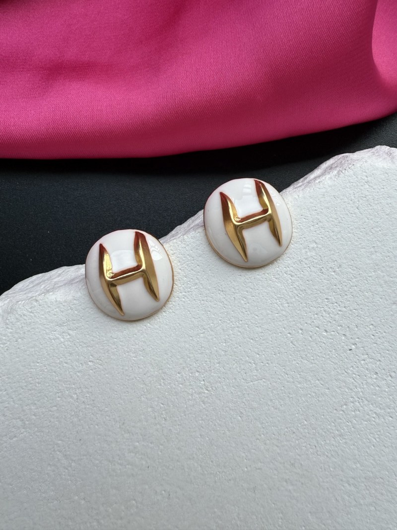 Серьги с золотым логотипом H на белом фоне Schiaparelli